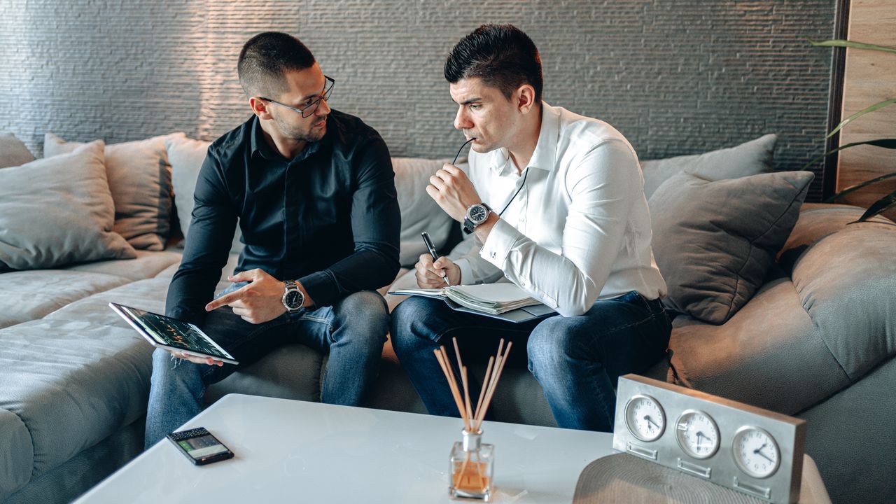 Two businessmen discussing ideas with digital tablet and notepad in a stylish office.
