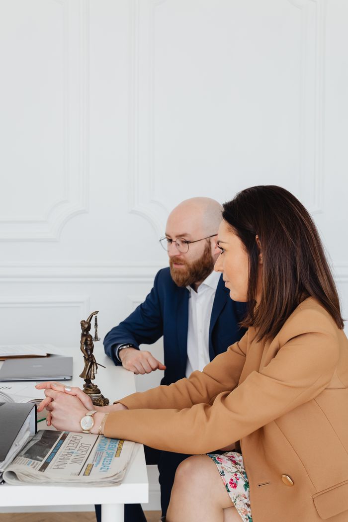 About Man and woman discussing legal documents indoors, featuring Lady Justice statue.