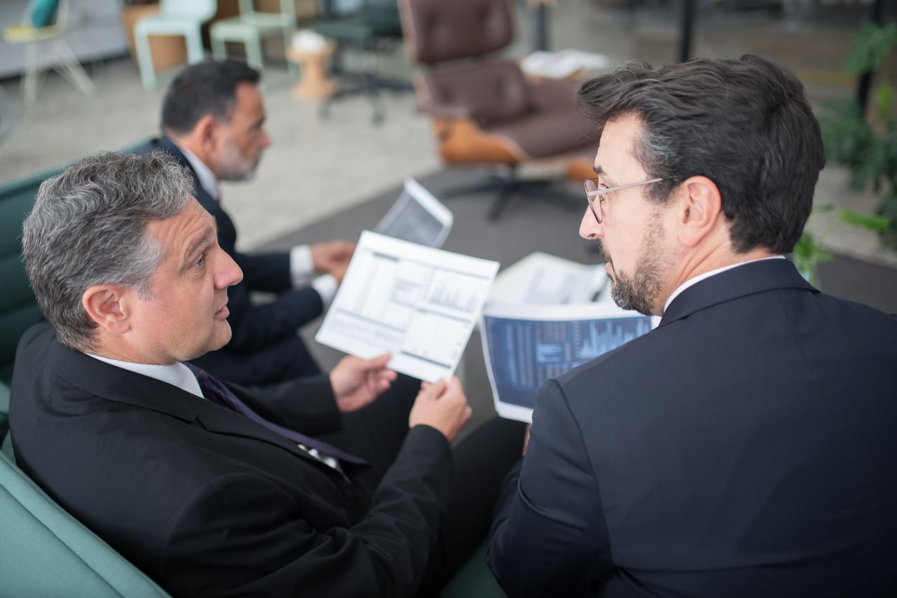 Three businessmen discussing financial documents in a modern office setting.